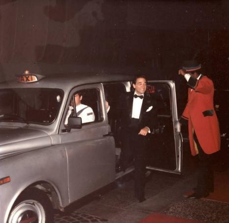 Man in tuxedo exiting vintage taxi with bellhop
