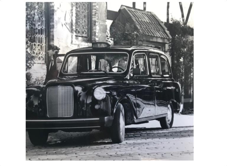 Vintage black London taxi on cobblestone street, black and white